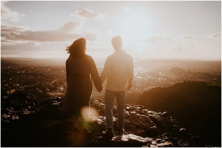 Couple holding hands at sunset on Arthur’s Seat overlooking the Edinburgh skyline.